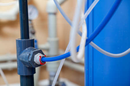 blue flexible plastic hose on a rigid pipe of a household water purification system. near light...