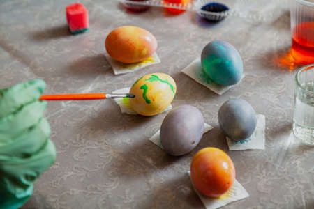 Hands in rubber blue gloves hold an egg and paint brush. Homemade painted Easter eggs and glasses...