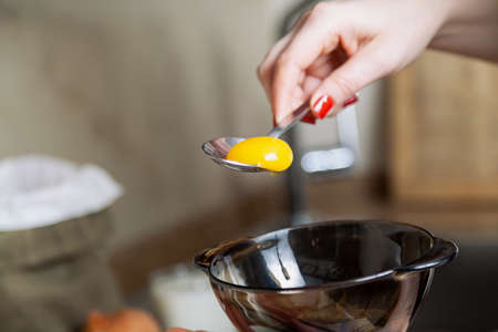 female hand pours the yolk of a chicken egg from a spoon into a glass bowlの写真素材