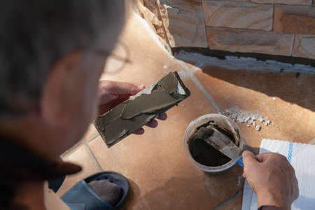 We install the tiles on the wall of the house. A hand applies a layer of special glue to flat...
