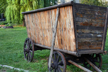 Vintage cart with high sides made of flat wooden planks stands on wooden wheels on green grass