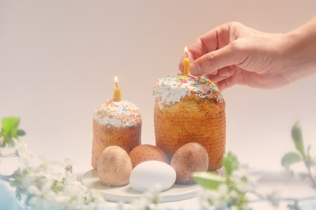 Two Easter cakes and eggs stand on a round stand on a white background. Candles are inserted into...
