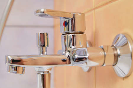 Chrome plated lever-type metal faucet mounted on the wall above the bathroom close-up