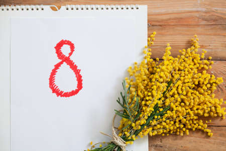 March 8 women holiday. A bouquet of yellow mimosa with green leaves lies on wooden boards. Nearby...