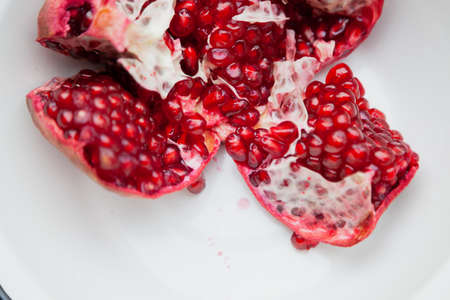 broken pomegranate with ripe red grains lies in a white bowlの写真素材