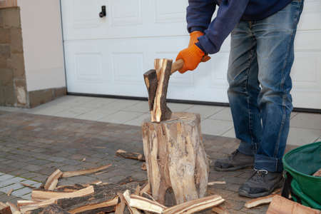 Orange-gloved hands chop a log on a stump with an ax. Behind the white garage doorの写真素材