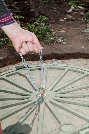 Hand pulls the metal chain on a round manhole cover close-upの写真素材