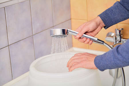 hand holds a shiny shower head and pours water into a round plastic container. close-upの写真素材