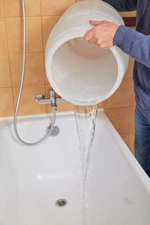 Hand poured water from a round plastic barrel into a bathtub. close-up