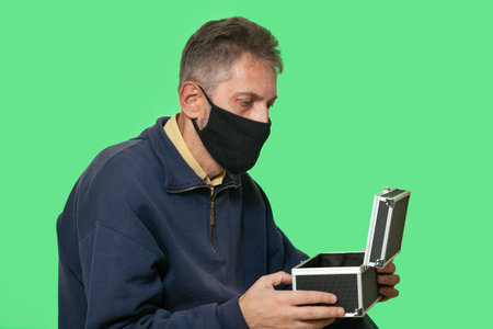 secret mission. A man in a black protective mask opens a case isolated on green chroma key backgroundの写真素材