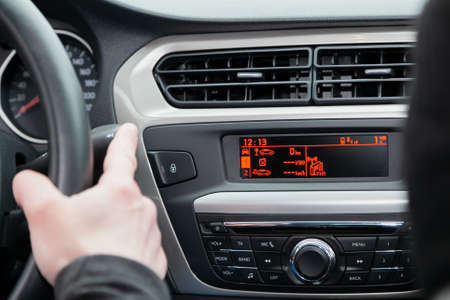 Various digital indicators are visible on the dashboard of the car. The driver's hand holds the...