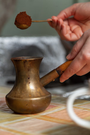 We brew natural coffee. Woman hand pouring ground coffee into a brass turk with a spoonの写真素材
