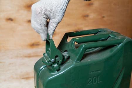 hand in a work glove opens the lid on a green metal canister against a background of light plywood close-upの写真素材
