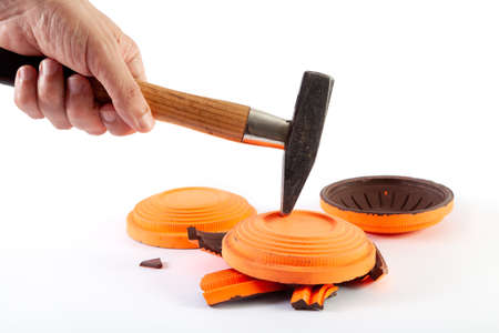 Test of strength. A hand breaks a clay target with a hammer. There are several whole orange plates on the back. close-upの写真素材