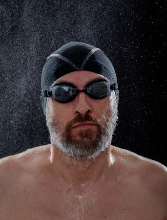 Portrait of a man in swimming goggles and a cap on a black background. Small drops of water are visible in the backgroundの写真素材
