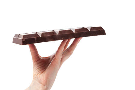 The left female palm holds on her fingers a large bar of dark chocolate on a white background