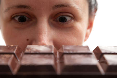 A young woman devours with her eyes a huge bar of dark chocolate close-up. The sight of chocolate...