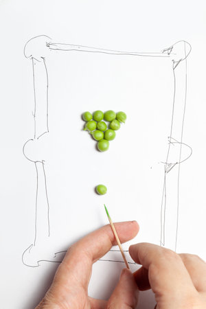 Green pea kernels in the form of a pyramid for playing billiards. The billiard table is drawn in a primitive style. Fingers imitate hitting the ball with a wooden toothpickの写真素材