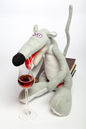symbol of 2020, a cute gray rat with a long tail sits on a stack of books on a white background close-up. A large red tongue inserted into an elegant glass cup with a long stemの写真素材