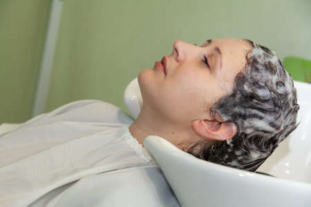 A young pretty woman threw her head back on a special sink for ready in a hairdressing salon....