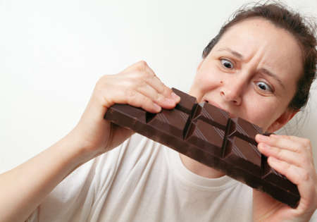 Young woman with an effort breaks a large bar of dark chocolate with two hands on a white backgroundの写真素材
