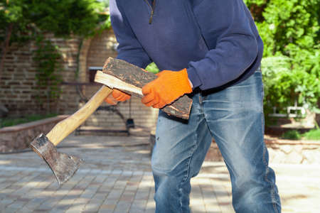 We prepare firewood for the barbecue. Hands in orange gloves chop a log on a stump with an ax on a sunny dayの写真素材