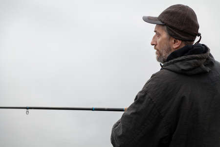 Portrait of a fisherman in profile. A man in a jacket catches fish with a spinning rod on the shore...