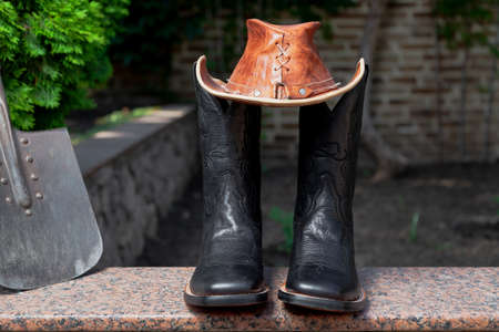 Attributes of american farmer. Black men's cowboy-style leather boots stand on a granite walkway. On...