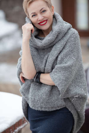beautiful blonde with a short haircut in a warm sweater is standing in the winter yard. In the background is a carの写真素材