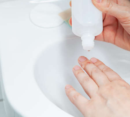 The right hand pours antiseptic on the injury on the middle finger of the left hand. The procedure is carried out under sterile conditions over a white tiled sinkの写真素材