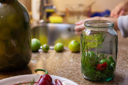 Preparation for preserving vegetables. A glass jar with green dill leaves and a tomato stands on the...