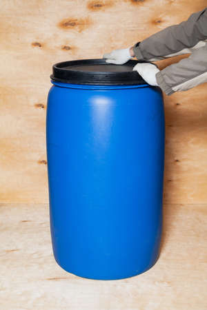 Hands in white gloves close a black lid on a blue round plastic container against a background of light plywoodの写真素材