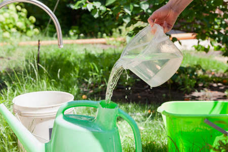 Irrigation preparation. Hands pour water into a plastic watering can for watering the garden. A jet of water pours out of a transparent plastic containerの写真素材