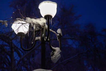 two retro-style circular outdoor lights shine with a beautiful white light. There is snow on topの写真素材