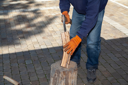 We prepare firewood for the barbecue. Hands in orange gloves chop a log on a stump with an ax on a sunny dayの写真素材