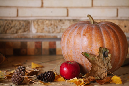 Halloween is coming. A large orange pumpkin is on the shelf. Nearby is a beautiful red apple, pine cones and yellow leaves.の写真素材