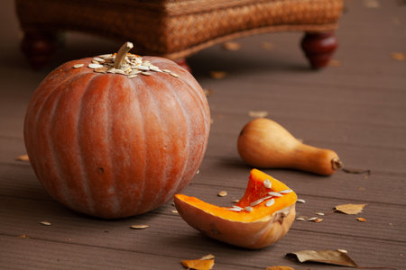 Autumn still life with pumpkins. A large round pumpkin and fallen leaves of trees lie on the boards. Nearby is a cut pumpkin and an elongated pumpkinの写真素材