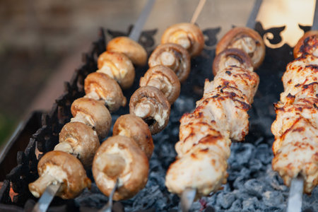 Grilling a barbecue. On a metal grill lies a row of skewers with mushrooms and pieces of meatの写真素材