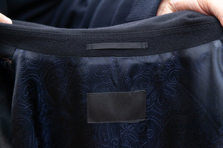 The inside of a new coat. Rectangular gray satin-lined label inside the coat. Embroidered pattern on...