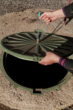 Hand pulls the metal chain on a round manhole cover close-upの写真素材