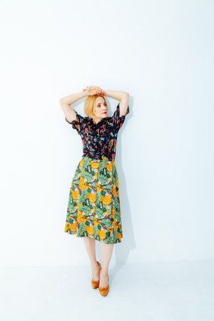 Pretty blonde with short hair in a yellow skirt with a green floral print stands on a white backgroundの写真素材