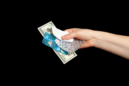 Buying drugs for dollars. One hundred dollar bill and empty pill blisters in hand on black backgroundの写真素材