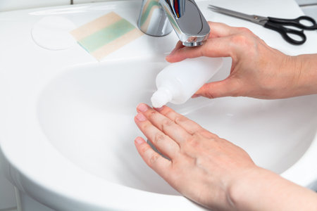 The right hand pours antiseptic on the injury on the middle finger of the left hand. The procedure is carried out under sterile conditions over a white tiled sinkの写真素材
