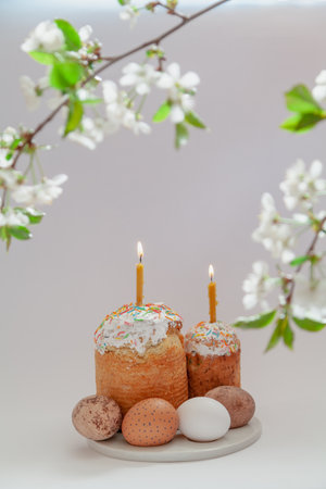 Easter still life. Two Easter cakes and eggs stand on a white background. Burning candles are inserted into the cakes. Top view of a tree branch with white flowersの写真素材
