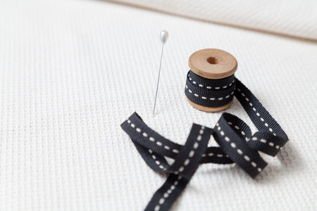 A black ribbon is wound on a wooden reel with a white line in the middle. The reel stands on a white...