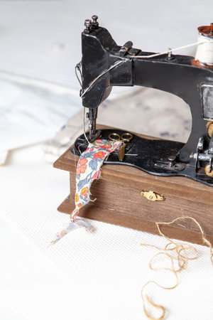 Vintage sewing machine with a spool of white thread stands on a white fabric with blue drawings