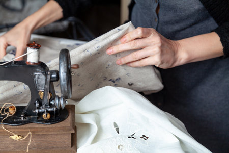 Woman hands are holding a piece of folded cloth close-up. In the foreground is a hand sewing machine