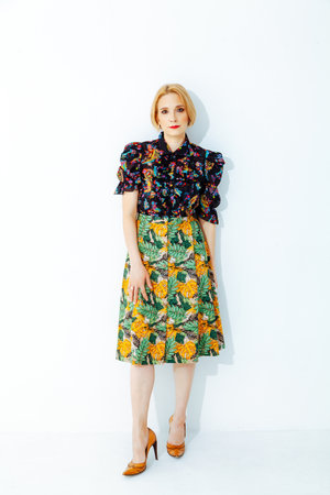 Pretty blonde with short hair in a yellow skirt with a green floral print stands on a white backgroundの写真素材