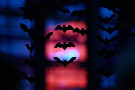 Black silhouettes of bats are vertically arranged on a blurred red and blue background. Garland for...