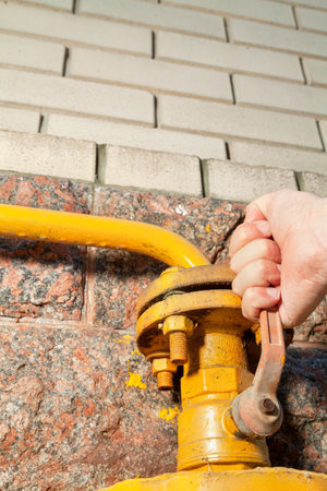 A hand opens a faucet at a natural gas supply to a house. Yellow metal protective cover installed at the bottom of the wallの写真素材